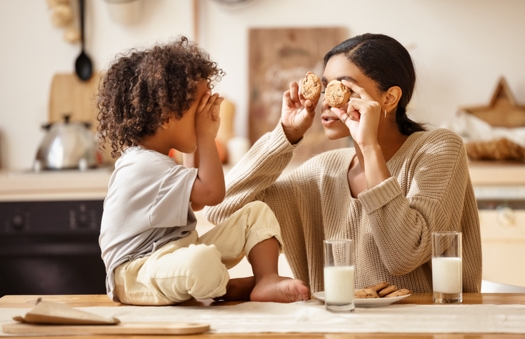 happy african american family: mother and little son eat cookies with milk at home