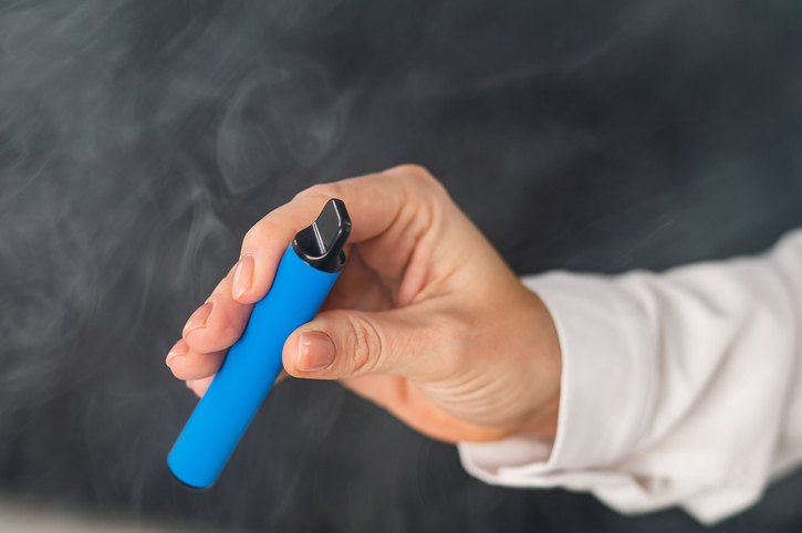 Caucasian woman smokes disposable vape on black background. Alternative device for smoking. Close-up of a female hand