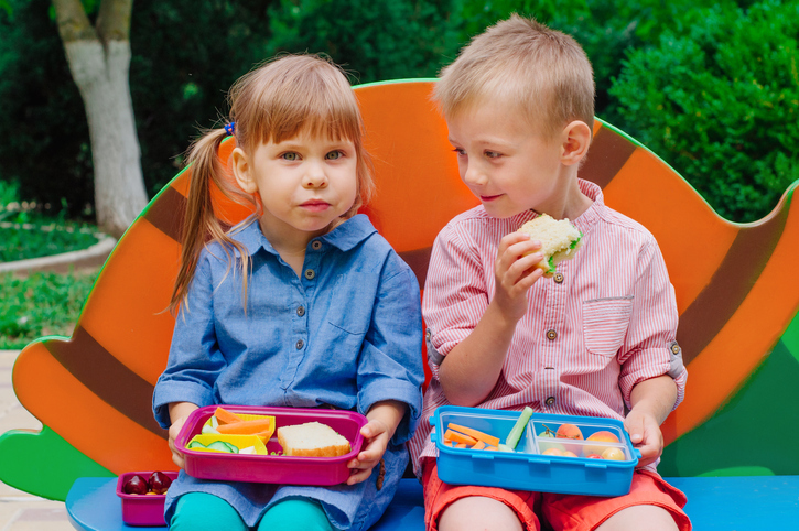 Elementary school students boy and girl eating lunch from lunch box sitting outdoor